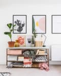 Console table with plants, books, and decor under three framed prints in a bright living room.