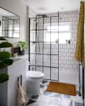 Modern bathroom with black-framed shower, white subway tiles, potted plants, and geometric floor tiles.
