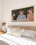 Bedroom with a wooden bed, white bedding, abstract art, and a shelf with candles and decor.