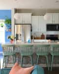 Kitchen with white cabinets, stainless steel appliances, blue accent wall, and mint green bar stools at a patterned island.