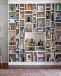 Woman sitting on stairs beside a large, filled bookshelf with books, decor, and a small bar setup.