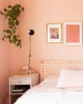Bedroom featuring pale peach walls, famed art, a bed with white and pale peach bedding, and one either side of the bed matching white side tables and plug-in sconce lights