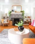 Living room with orange sofa, patterned fireplace, round coffee table, plants, and wooden sideboard.