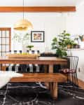 Dining room with wooden table, black and white checkered bench, gold pendant light, and various potted plants.
