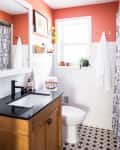 Bathroom with coral walls, black countertop, wooden vanity, patterned floor tiles, and plants on the windowsill.