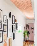 Hallway with framed art on white walls, patterned ceiling, potted plants, and a woven rug on wooden floor.
