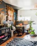 Eclectic living room with gray sofa, geometric rug, hanging plants, and a wall tapestry.
