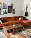 Living room with orange velvet sofa, mid-century tables, colorful rug, and concert artwork on wall