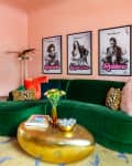 Green velvet sofa with leopard print cushions, gold coffee table, and pop art posters on pink walls in a vibrant living room.