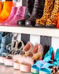 Colorful and eclectic collection of boots and high heels on display shelves, featuring glitter, spikes, and animal prints.