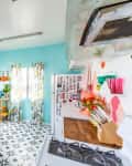 Bright kitchen with floral curtains, hanging plants, white cabinets, and colorful decor.