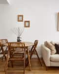 Dining area with round wooden table, four chairs, beige sofa, and framed wall art.