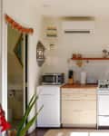 Small kitchen with light wood cabinets, gas stove, microwave, colorful pendant light, and open door to a bathroom.