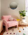 Cozy living room with a pink armchair, shell pillow, potted plant, colorful rug, and wall art.