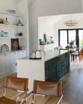 Open kitchen with white cabinets, brown leather chairs, and a long island leading to a dining area with a chandelier.