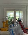 Living room under renovation with covered furniture, a ladder, and a white brick fireplace.