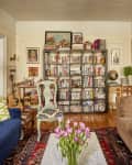 Cozy living room with blue and brown sofas, colorful cushions, bookshelf, framed art, and a vase of pink tulips on a table.