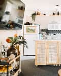 Cozy kitchen with wicker cabinets, black and white backsplash, plants, and a small dining table with wooden chairs.