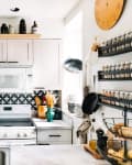 Cozy kitchen with white cabinets, black and white backsplash, espresso machine, spice racks, and decorative shelves.
