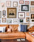 Brown leather sectional sofa with patterned pillows, a throw, and a gallery wall of framed art and photos above.