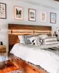 Brass sconces on either side of a large bed with a rustic wood bed frame, with art prints above the bed