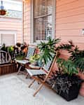 Small porch with pink siding, patterned chairs, and various potted plants.