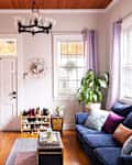 Cozy living room with blue sofa, colorful cushions, potted plants, shoe rack, and wall-mounted TV.
