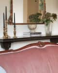 Vintage pink sofa with blue cushions, ornate mirror, brass candlesticks, and floral lamp in a cozy living room.