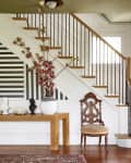 Entryway with a wooden console table, decorative busts, a vase with pink flowers, and a striped wall under a staircase.