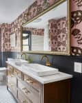 Bathroom with pink floral wallpaper, double sinks, gold faucets, large mirror, and hexagonal floor tiles.