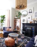 Cozy living room with navy sofas, patterned rug, plants, and eclectic decor around a black fireplace.