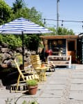 Backyard with blue house, yellow chairs, striped umbrella, string lights, and a grill on a patio.