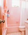Pink bathroom with tiled walls, pink bathtub, matching sink, white shower curtain, and yellow flowers on the counter.