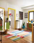 Colorful kitchen with yellow cabinets, striped rug, spiral staircase, and two dogs lounging on the floor.