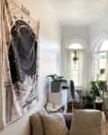 Cozy living room with tapestry, plants, white dresser, and arched windows with sheer curtains.