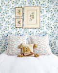 Floral-themed bedroom with patterned wallpaper, colorful pillows, framed art, and bedside lamps.