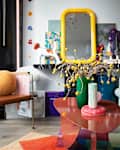 Colorful living room with eclectic decor, including a yellow mirror, abstract art, and a table with vibrant vases and flowers.