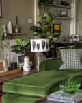 Green velvet sofa with patterned cushions, tulips in a vase, and plants in a cozy living room with dining area in the background.