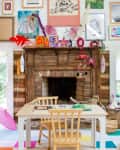 Colorful playroom with a white table, wooden chairs, bunk bed, and art-filled mantel, featuring toys and vibrant decor.