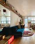 Cozy living area featuring a blue sofa, wooden flooring, a round dining table, and plants near large windows.