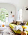 Living room with green sofa, patterned pillows, round coffee table, large plant, and arched window with decorative glass.
