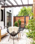 Outdoor patio with wooden sofa, black chairs, potted cactus, and string lights under a pergola.