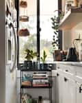 Cozy kitchen corner with a white refrigerator, gas stove, and a black cart holding cookbooks and plants, featuring a window view.