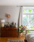 Bedroom with wooden dresser, potted plants, and a window with green stained glass accents.