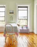 Bright living room with a wooden piano, dining table, floral tablecloth, and large windows overlooking greenery.