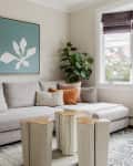 Gray sofa with assorted pillows, abstract wall art, wooden stump coffee tables, and a large plant by a window.
