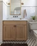 Bathroom with wooden vanity, white subway tiles, round mirror, brass sconces, and a potted plant on the toilet.