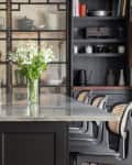 Modern kitchen with marble island, black cabinets, open shelving, and a vase of white flowers.