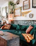 Eclectic living room with green velvet sofa, vintage trunk coffee table, patterned pillows, and wall art.