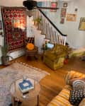 Cozy living room with colorful rugs, vintage armchairs, wall art, and a glass coffee table near a staircase.